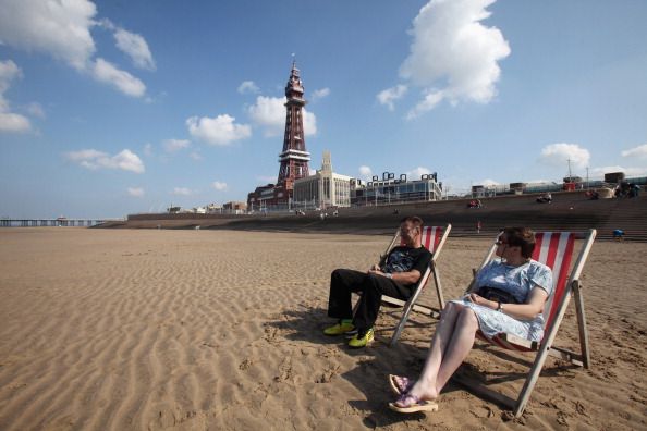 BLACKPOOL, ENGLAND - SEPTEMBER 01: Holidaymakers sit on the beach next to the refurbished Blackpool Tower on September 1, 2011 in Blackpool, England. After a 20million GBP refurbishment the iconic seaside Blackpool Tower opened today to the general public. The observation deck at the top of the tower becomes the Blackpool Tower Eye and features a skywalk made of glass overlooking the sea and the promenade. The opening is part of Blackpool's 250million GBP regeneration project. (Photo by Christopher Furlong/Getty Images)