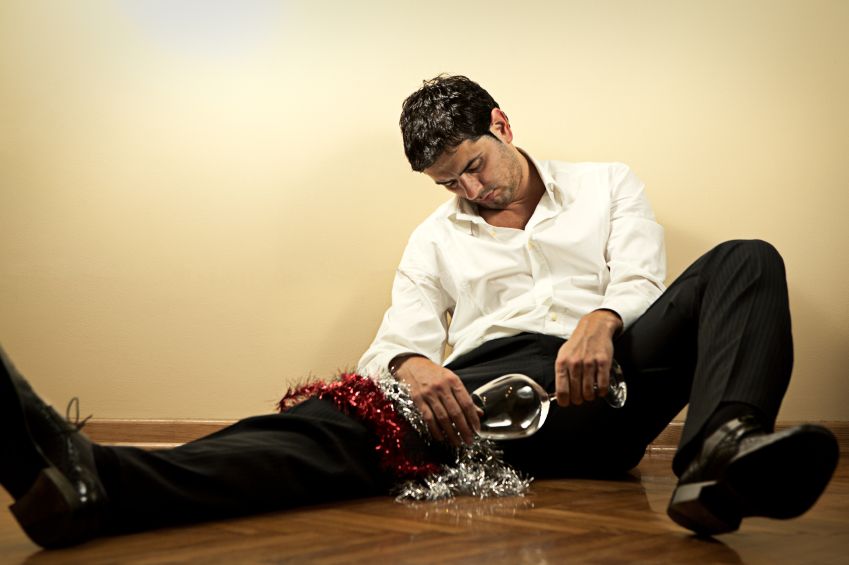 Drunk businessman sitting on the floor with empty wine glass after office party