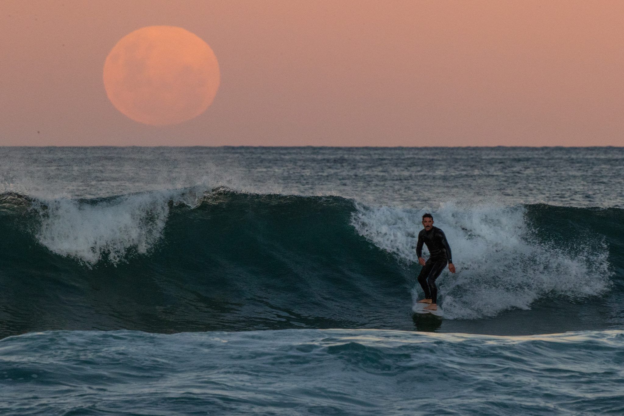 SYDNEY, AUSTRALIA - MAY 26: A surfer rides a wave as a super blood moon rises above the horizon at Manly Beach on May 26, 2021 in Sydney, Australia. It is the first total lunar eclipse in more than two years, which coincides with a supermoon. A super moon is a name given to a full (or new) moon that occurs when the moon is in perigee - or closest to the earth - and it is the moon's proximity to earth that results in its brighter and bigger appearance. (Photo by Cameron Spencer/Getty Images)